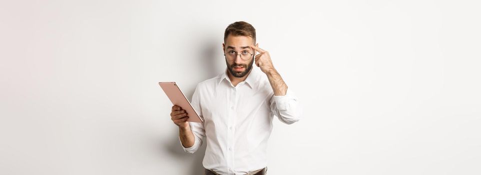 Displeased employer scolding staff while checking report on digital tablet, pointing at head and looking disappointed, standing over white background.