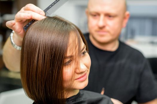 Young caucasian brunette woman having her hairstyling by a male hairdresser at a parlor