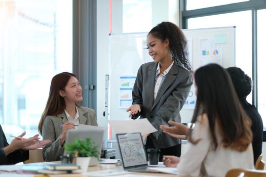 Asian business woman leader in a meeting with her multi-ethnic colleagues at the office presenting sales data or forecast for a project.