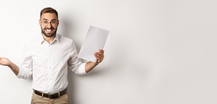 Awkward manager showing document and shrugging, looking guilty of mistake, standing over white background.