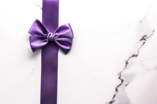 Happy holidays, festive decoration and brand sale promotion concept - Purple silk ribbon and bow on luxury marble background, holiday flatlay backdrop