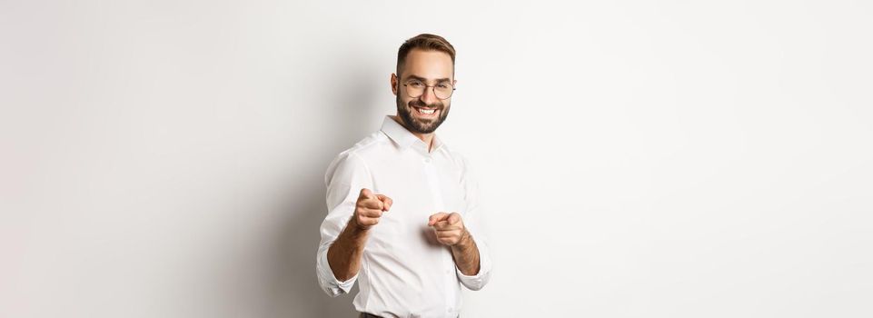 Confident businessman smiling, pointing fingers at you, congrats or praise gesture, standing over white background.