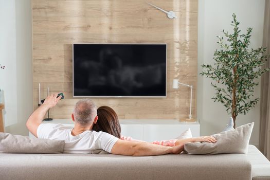 cheerful couple turns on the TV while lying on the sofa in the living room.