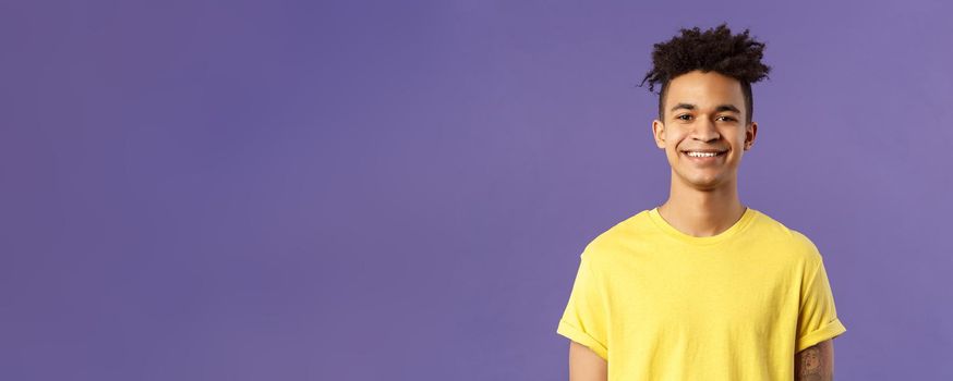 Close-up portrait of nice, friendly-looking hispanic male student in yellow t-shirt, grinning delighted, look upbeat happy and positive, standing enthusiastic with beaming smile purple background.