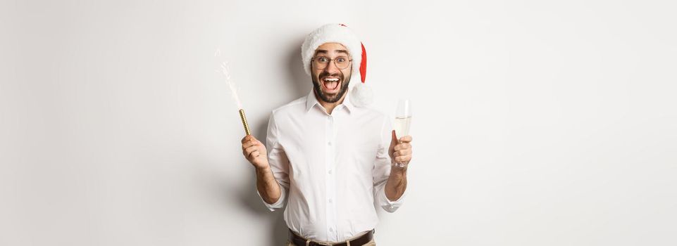 Winter holidays and celebration. Happy guy in Santa hat rejoicing at New Year party, drinking champagne and shouting of joy, white background.