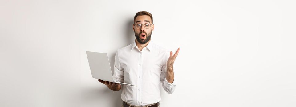 Business. Man holding laptop and looking amazed, surprised with website, standing over white background. Copy space