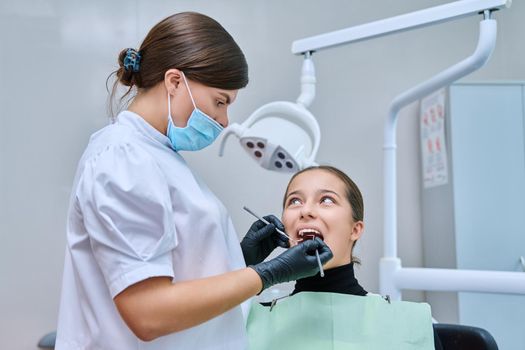 Young teenage female at dental checkup in clinic. Teenage girl sitting in chair, doctor dentist with tools examining patient's teeth. Adolescence, hygiene, dentistry, treatment, dental health care