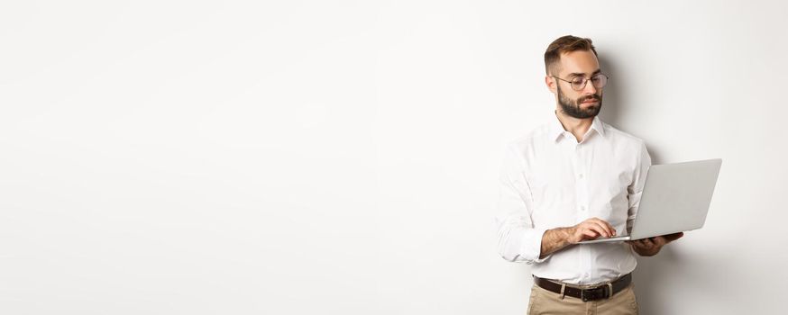 Business. Serious manager working on laptop, standing over white background. Copy space