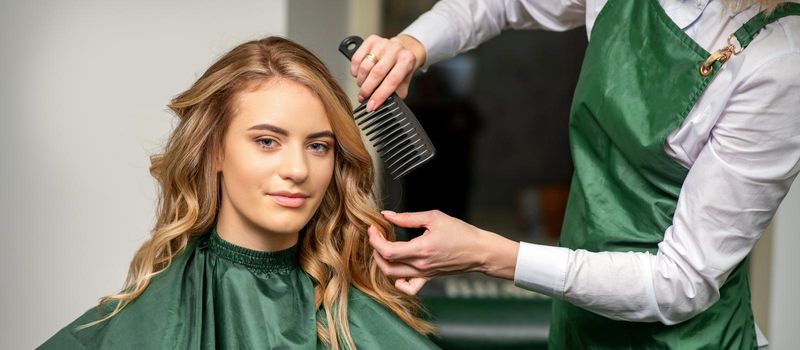 Hairdresser making hairstyling for the woman while combing with hairbrush, comb in a hair salon