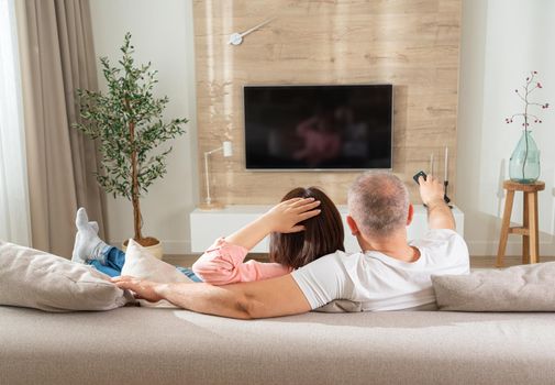 relaxed couple turn on tv while lying on sofa in living room.