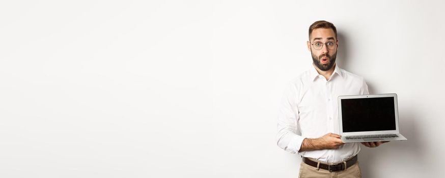 Amazed businessman showing laptop screen, standing against white background.