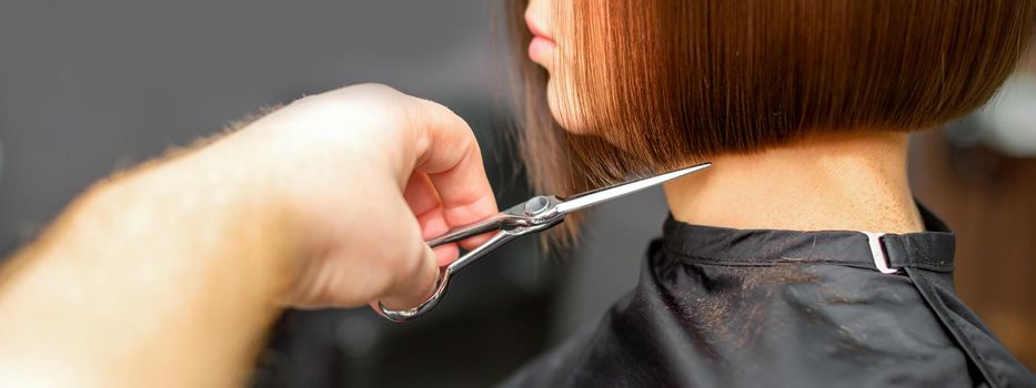 Woman having a new haircut. Male hairstylist cutting brown hair with scissors in a hair salon