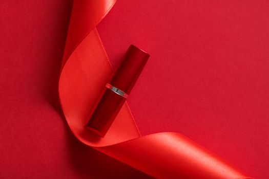 Cosmetic branding, glamour lip gloss and shopping sale concept - Luxury lipstick and silk ribbon on red holiday background, make-up and cosmetics flatlay for beauty brand product design