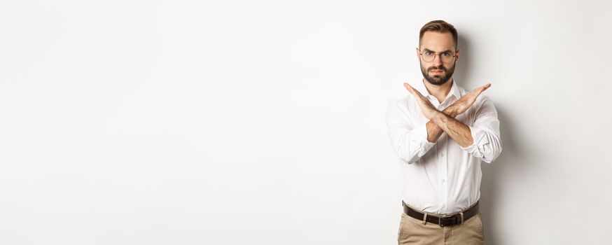 Angry businessman frowning and showing cross, stop you, telling no and prohibit something, standing over white background.