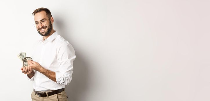 Successful business man counting money and smiling, standing against white background and looking satisfied.