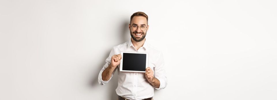 Shopping and technology. Handsome man showing digital tablet screen, wearing glasses with white collar shirt, studio background.