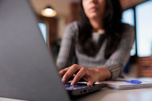 Business woman working on report at home, typing research information on laptop and browsing internet website. Searching data to create professional report and send email. Close up.