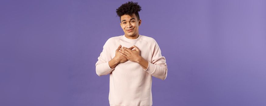 Portrait of touched silly young man left speechless and flattered, sobbing as being hit right into heart with dear warm words and praises, pleased standing purple background.