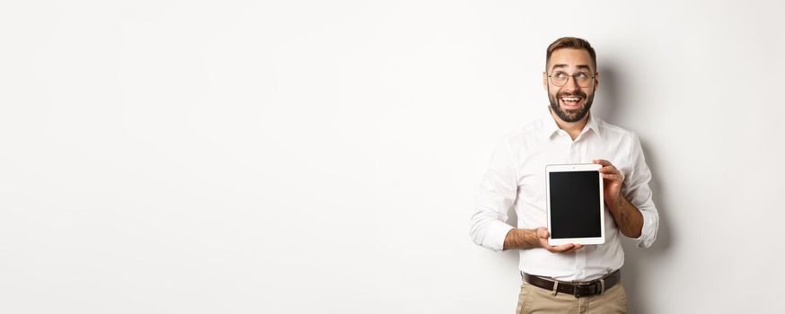 Shopping and technology. Thoughtful man showing digital tablet screen, looking at upper left corner and thinking, standing over white background.