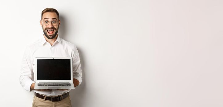 Excited businessman showing something on laptop screen, standing happy over white background.