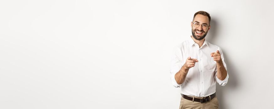 Satisfied businessman pointing fingers at camera, praising you, approve or like something, white background.