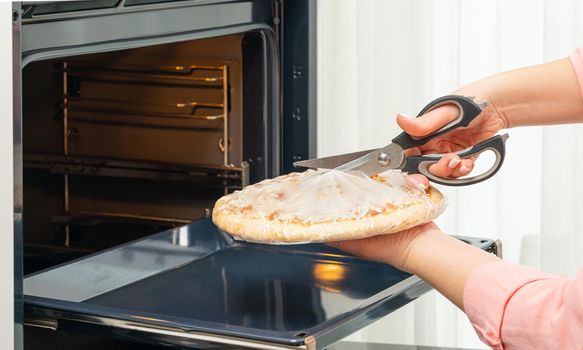 Woman's hands with scissors cut a package of pizza close-up.