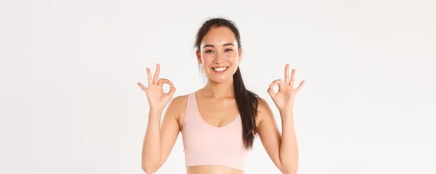 Sport, wellbeing and active lifestyle concept. Close-up of smiling, satisfied asian sportswoman recommend gym or yoga classes, showing okay gesture, pleased with perfect online coach.