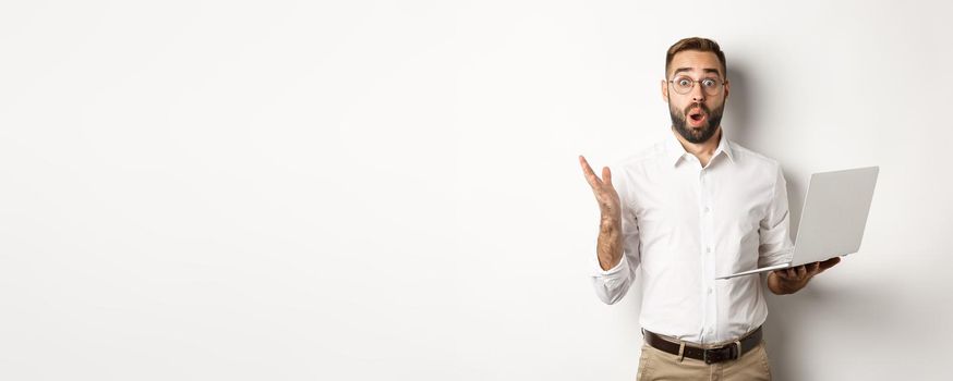 Business. Man holding laptop and looking amazed, surprised with website, standing over white background. Copy space