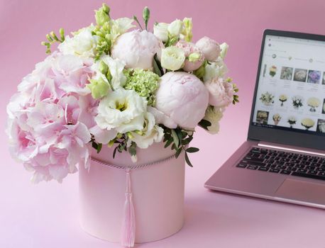 bouquet of flowers in a box close-up, against the background of an open laptop. Selective focus. Hydrangea, roses and peonies on a pink background. home delivery concept, buying flowers online.