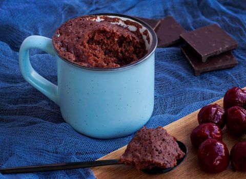 Brownie Chocolate Mug Cakes in cups on blue background. Cherries and chocolate. Fast cooking in microwave. Copy space. Piece of biscuit on a spoon. Chocolate cupcake in mug. Easy homemade concept