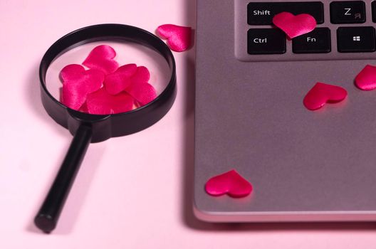 Red heart on the computer keyboard, magnifying glass with handle. Concept of searching for love on the internet, internet dating site, copyspace, place for text. Pink laptop on pink background.
