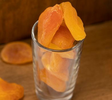 dried apricots are scattered from a glass on a wooden table. diet dessert. dried fruit orange. High quality photo