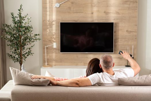 cheerful couple turns on the TV while lying on the sofa in the living room.