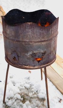 a rusty barrel with burning coals stands on the snow. Fire from a barrel. Winter bonfire concept. High quality photo