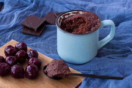 Brownie Chocolate Mug Cakes in cups on blue background. Cherries and chocolate. Fast cooking in microwave. Copy space. Piece of biscuit on a spoon. Chocolate cupcake in mug. Easy homemade concept