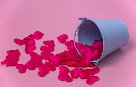 decorative hearts are scattered from a blue toy bucket on a pink background. The concept of giving a lot of love. High quality photo