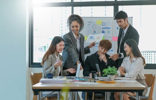 Asian business woman leader in a meeting with her multi-ethnic colleagues at the office presenting sales data or forecast for a project.