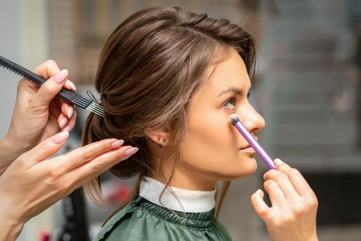 Makeup and hairstyle process. Makeup artist and hairdresser preparing young caucasian woman, working in tandem