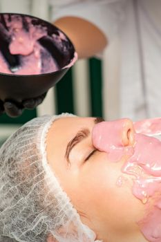 The cosmetologist applying an alginate mask to the face of a young woman in a beauty salon