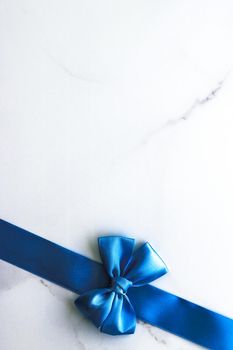 Happy holidays, festive decoration and brand sale promotion concept - Blue silk ribbon and bow on luxury marble background, holiday flatlay backdrop