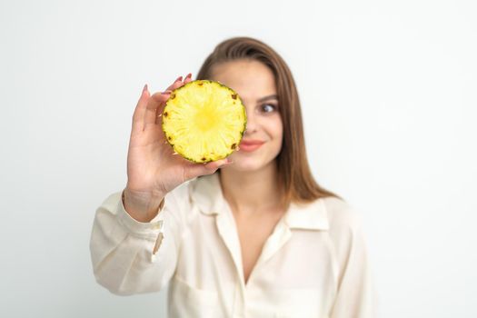 A young attractive pretty nice caucasian smiling woman holds ring slice pineapple covering her eye against a white background. Healthy eating concept