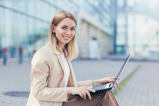 Cheerful woman working with laptop on the street near the office