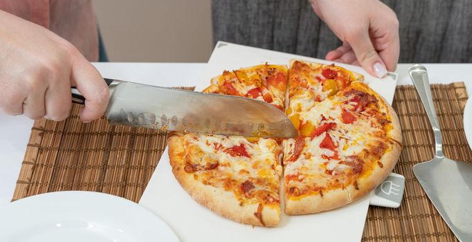girl cuts homemade pizza with a knife on the table.