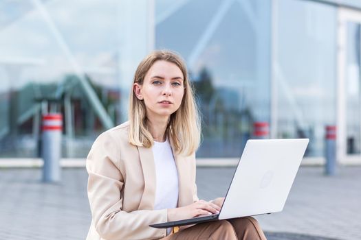 longing young woman sitting alone on street sidewalk on urban background modern building. Sad girl Student or businesswoman misses. Unemployed female lost her job, upset and lonely thoughtful, pensive