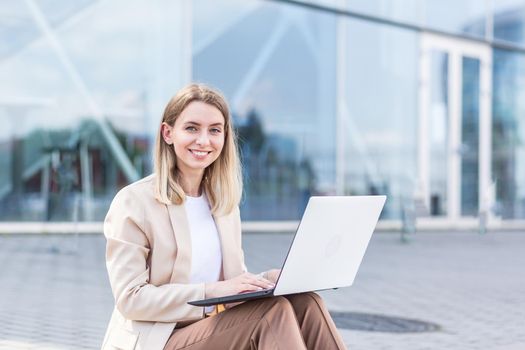 longing young woman sitting alone on street sidewalk on urban background modern building. Sad girl Student or businesswoman misses. Unemployed female lost her job, upset and lonely thoughtful, pensive
