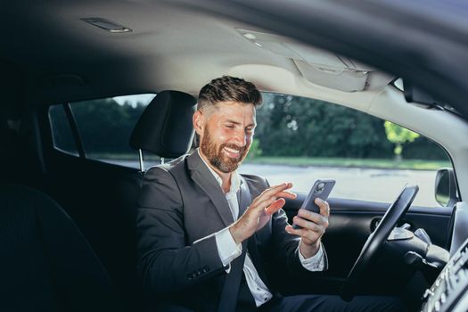 Excited emotional adult businessman driving car rejoicing online victory achievement lottery celebrating success screaming funny enjoying. Man holding his smartphone feeling happy Transportation.