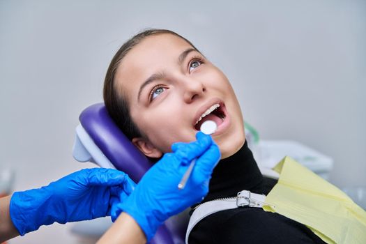 Young teenage female at dental checkup in clinic. Teenage girl sitting in chair, doctor dentist with tools examining patient's teeth. Adolescence, hygiene, dentistry, treatment, dental health care