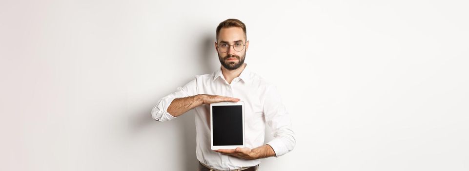 Confident bearded man showing digital tablet screen, demonstrating app, standing over white background.