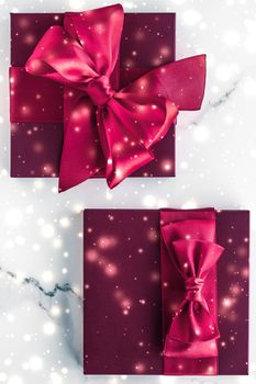 New Years Eve celebration, wrapped luxury boxes and cold season concept - Winter holiday gifts with cherry silk bow and glowing snow on frozen marble background, Christmas presents surprise