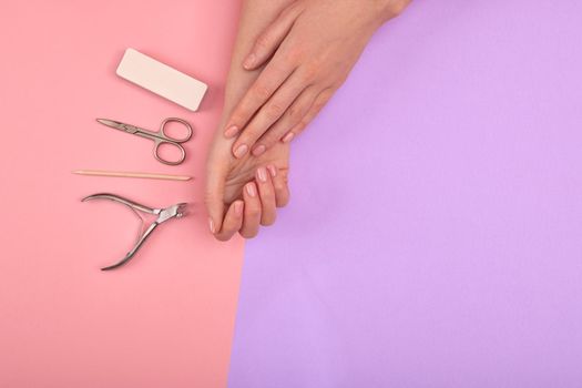 Hands with natural color manicure next to instruments for the procedure on pink purple background
